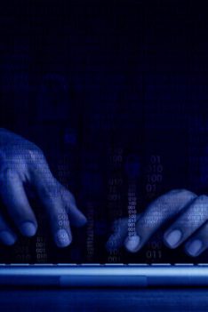 Cyberattack and internet crime, hacking and malware concepts. Digital binary code data numbers and secure lock icons on hacker’ hands working with keyboard computer on dark blue tone background.